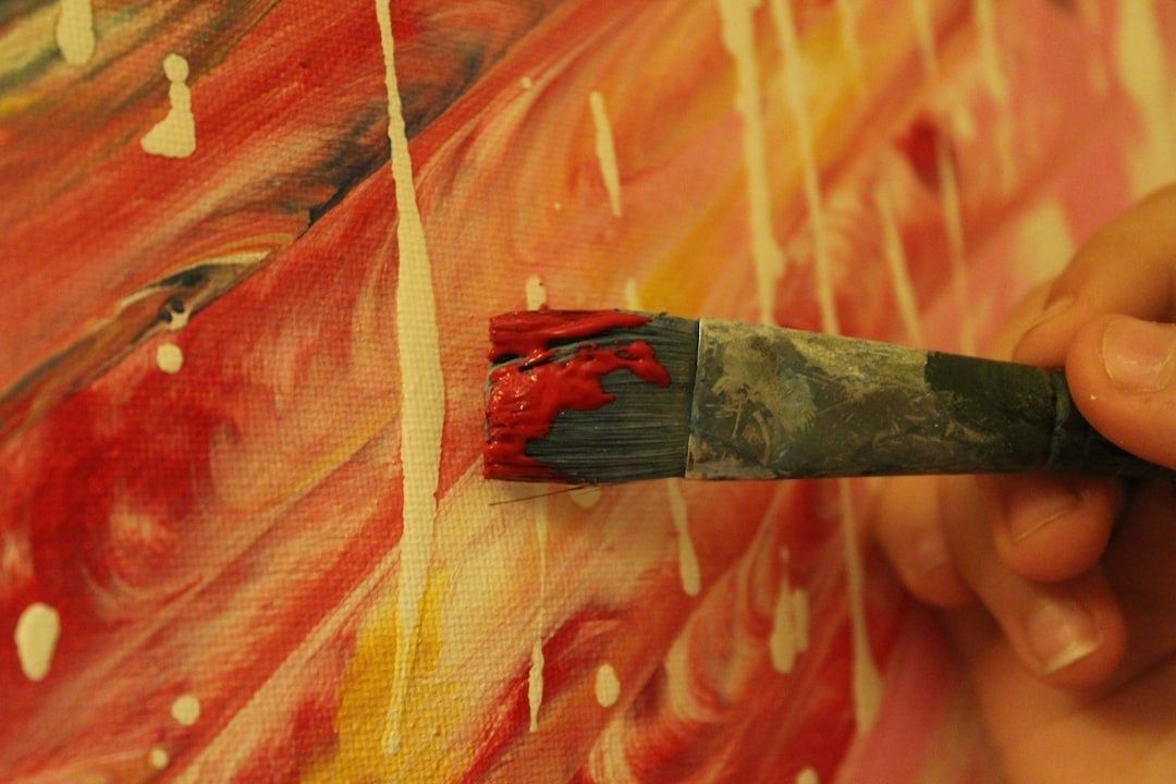 Penseel met rode verf op een felgekleurd abstract schilderij