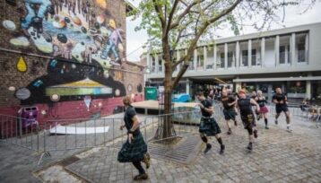 Straatkunstmuur naast een binnenplaats waar doedelzakspelers lopen