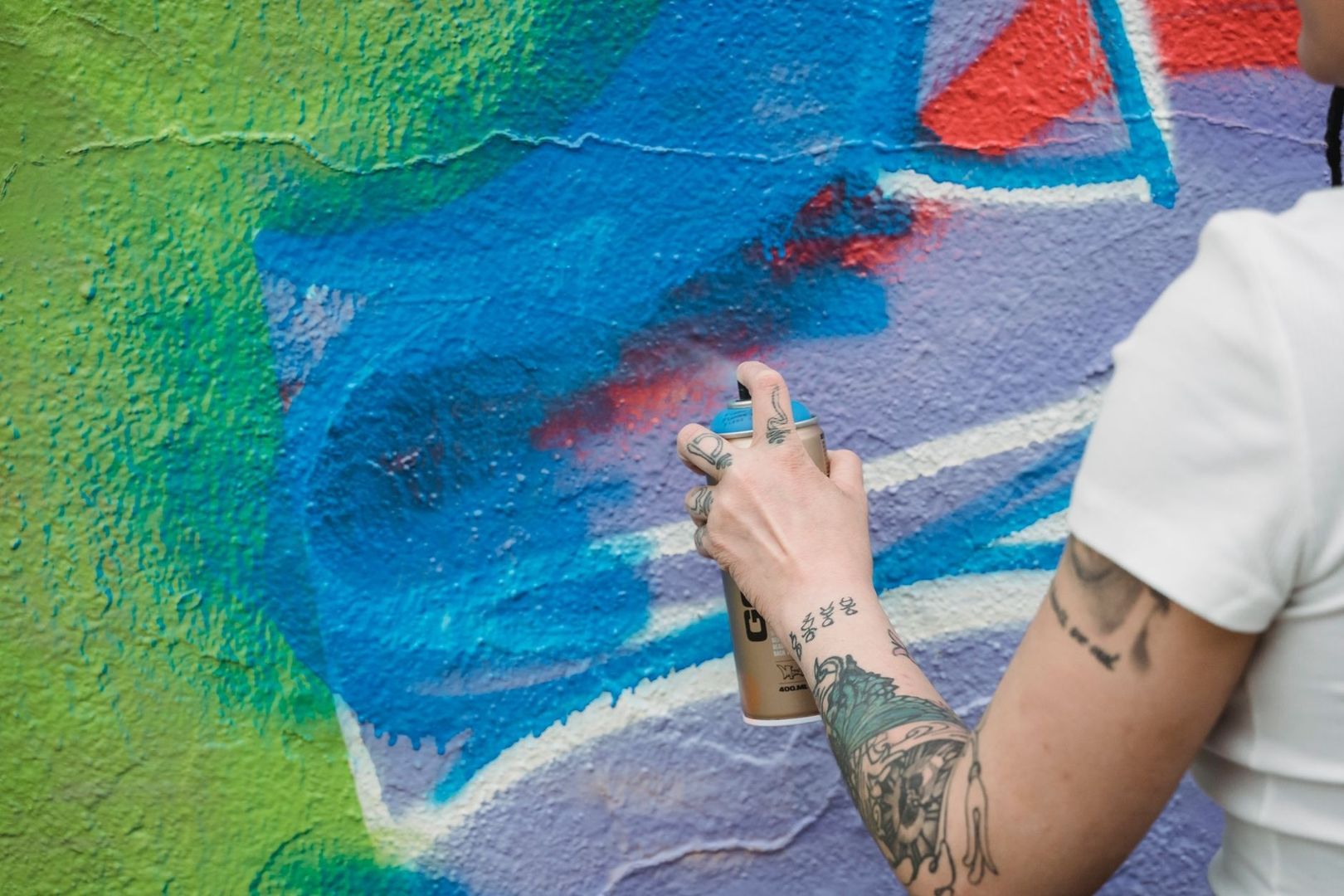 Getatoeëerde kunstenaar spuit blauwe verf op een kleurrijke muur
